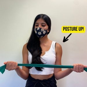 Girl performing resisted external rotation for both shoulders using a green band.